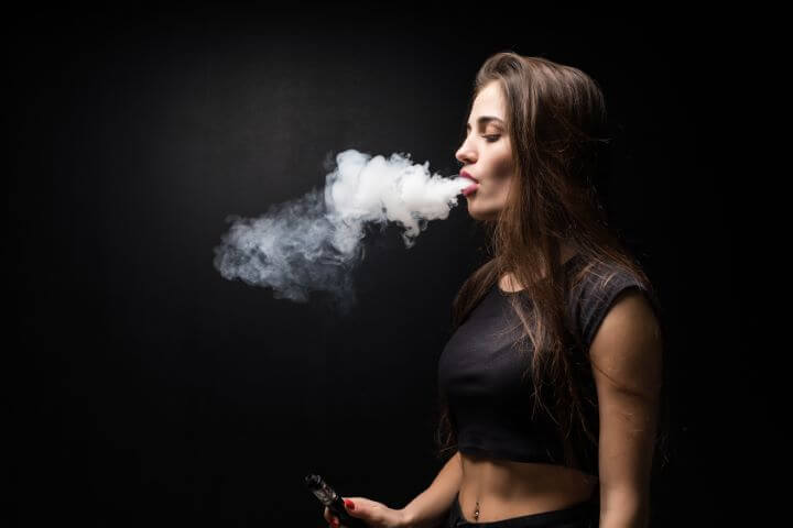 Young beautiful woman vaping e – cigarette on the Black background.